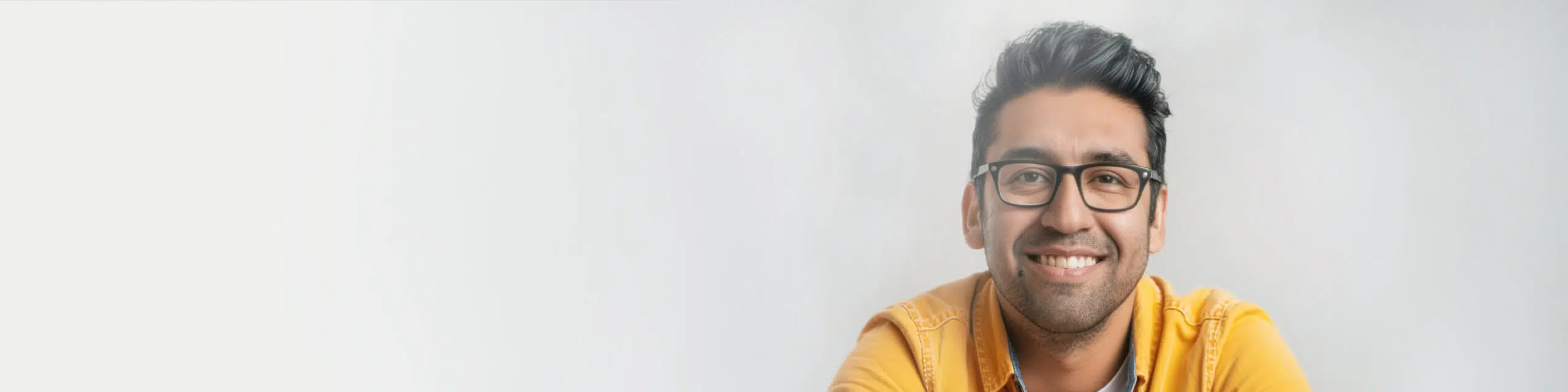 A person with short dark hair and glasses smiles at the camera. They are wearing a yellow shirt and are positioned against a plain light background.